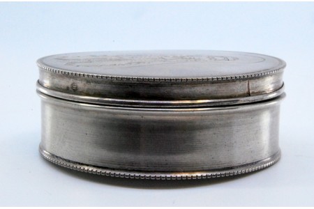 Caixa de comprimidos em prata de forma circular com imagem de Nossa Senhora de Fátima gravada na tampa amovível.